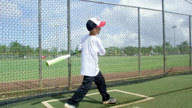 Slow motion of kid hitting ball at batting cages in baseball park
