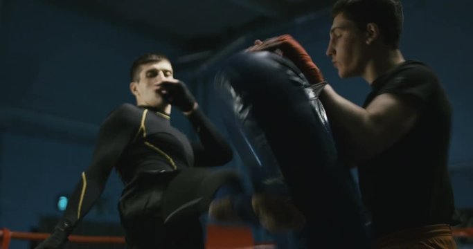 Coach holding boxing bag and training sportive man to attack and learn technique of Thai box.