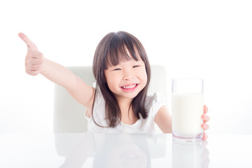 Little asian girl holding a glass of milk and showing thumb up over white background