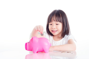 Little asian girl putting coin into pink piggy bank over white background