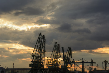 Fototapeta na wymiar Silhouette of port cranes against a dramatic sky at sunset.