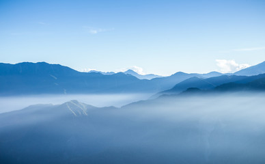 Obraz na płótnie Canvas Hazy blue mountains of Zhushan inside Alishan Recreation Area in Taiwan covered by fog during sunrise in morning with bright winter sky.