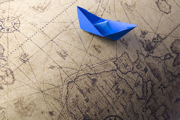 Blue paper ship isolated on old map background. Paper craft and origami. Paper ship on world map