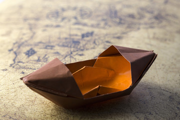 Blue paper ship isolated on old map background. Paper craft and origami. Paper ship on world map