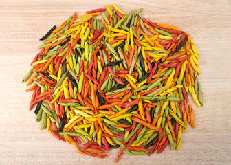 Pile of bright colorful hand rolled dry pasta made from vegetables on a light wood table. Healthy vegetarian Italian pasta.