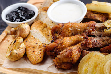 Mixed fresh grilled meat with onion, mushrooms and sauce on wooden cutting board. Assorted delicious barbecue meat with vegetables from summer BBQ. Healthy eating
