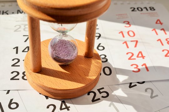 песочные часы стоят на листках отрывного календаря в лучах весеннего солнца