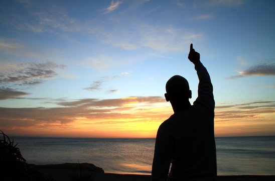 image of sunset with man with arms outstretched praying to god stock photo