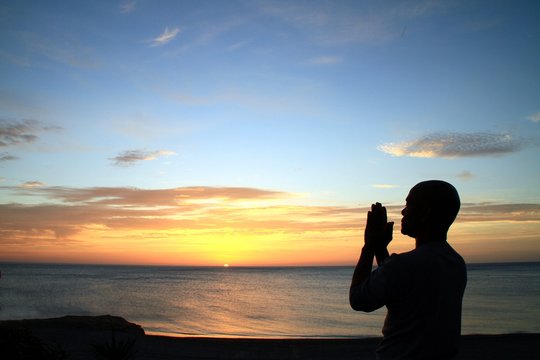image of sunset with man with arms outstretched praying to god stock photo