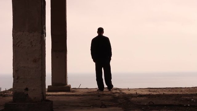 Sad lonely man standing alone on edge of abandoned construction. Silhouette of a sad man standing on the edge of a tall building