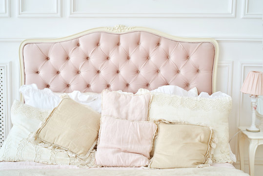 Large buttoned headboard of luxury bed, beige and pink pillows on it, copy space. Feminine bedroom in pink and white colors. Chesterfield style checkered soft headboard, diamond pattern