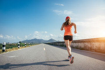 An asian woman athletic is jogging on the concrete road, she is warming her body and tideten her tying her shoes tightly fitting before workout.