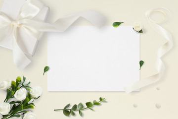 Letter, envelope and a present on pastel yellow background. Wedding invitation cards or love letter with chrysanthemums. Valentine's day or other holiday concept, top view, flat lay, overhead view.