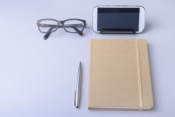 Business concept. Top view of kraft spiral notebook, glasses, smartphone and black pen isolated on background for mockup.