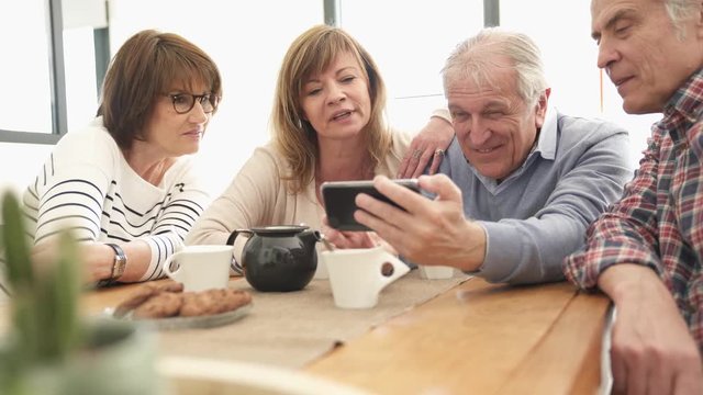 Group of senior friends looking at pictures on smartphone