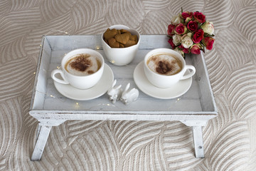 two cups of coffee on the table and cookies in the shape of a heart, two rabbits, a bouquet of roses and a garland