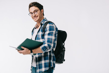 smiling handsome student holding copybook and looking at camera isolated on white