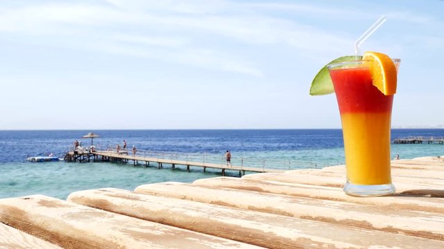 Red strawberry mousse and freshly squeezed mango juice with slices of fresh melon and orange on a wooden table on a blue and turquoise sea background or ocean on a beach on a sunny day