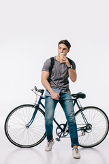 Fototapeta na wymiar handsome student drinking coffee and leaning on bicycle on white