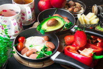 English health breakfast for two. Fried eggs with sausages in a frying pan with spices and fresh vegetables, cheese, nuts