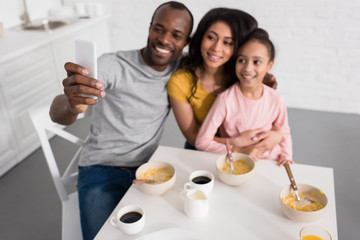 smiling young family taking selfie on kitchen while having breakfast