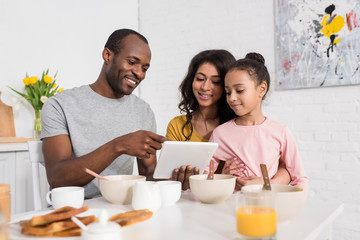 beautiful young family using tablet on kitchen while having breakfast