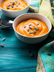 Creamy pumpkin soup in white bowls on green wooden table