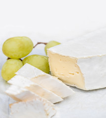 Fresh Brie cheese with slices and grape on white rustic on a wooden board. Brie type of cheese.  Camembert cheese.