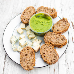 Guacamole, cheese and slices of bread over white wooden background with copy space. Picnic, lunch or dinner concept. Food and drink, top view