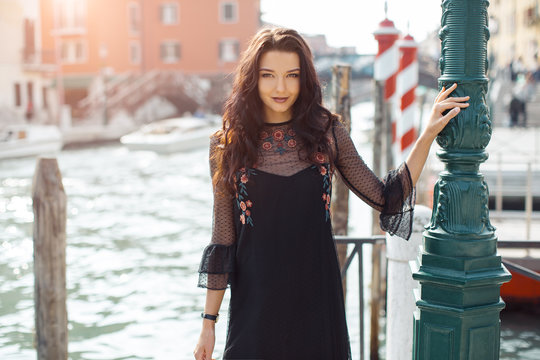 Attractive young romantic woman standing on the pier against beautiful view on venetian chanal with boats and gondolas in Venice, Italy. Travel tourist girl on vacation walking happy by Grand Canal