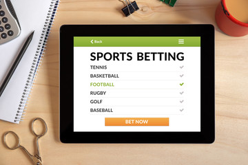 Sports betting concept on tablet screen with office objects on wooden desk. All screen content is designed by me. Top view