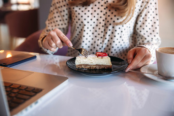 Girl eating cake in a cafe. Blonde in polka-dot shirt with laptop