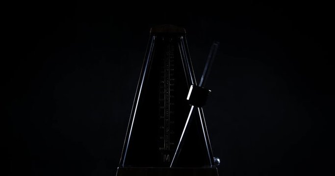 Slow motion shot of vintage metronome with golden pendulum beats slow rhythm on the dark background