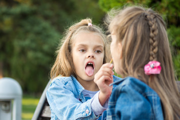 One girl treats another girl with her lollipop