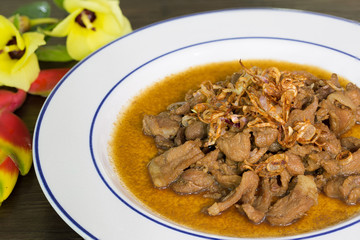 Stir pork slice with coconut sugar sprinkle with fried shallot slice (Sweet pork) in white dish Thai food, Decorated dish with flower for beautiful.