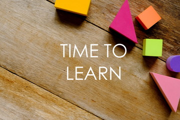 Top view of colorful soft blocks on wooden background written with 'TIME TO LEARN'.