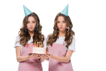 attractive young twins holding birthday cake and looking at camera isolated on white