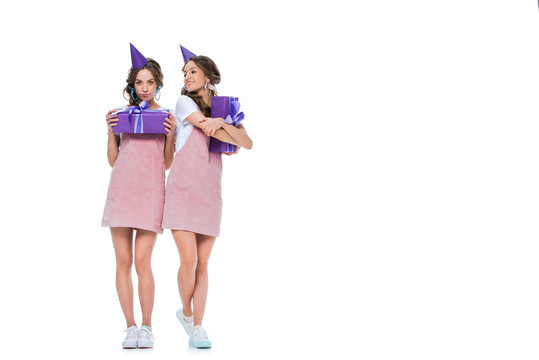 beautiful young twins in birthday caps holding presents isolated on white