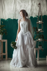 Beautiful model wearing white wedding dress is posing in an interior studio
