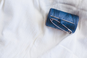 Blue thread spool with sewing needle and pin on white cotton cloth