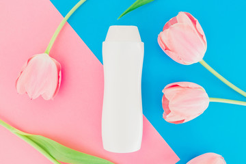 Shampoo and tulips flowers on pink and blue background. Flat lay, top view