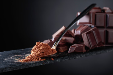 Broken chocolate pieces and cocoa powder on black background.