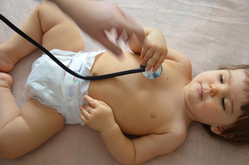Obraz na płótnie Canvas Pediatrician examining baby girl. Doctor using stethoscope to listen to kid back checking heart beat.