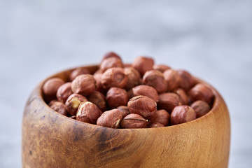 Hazelnuts in wooden bowl on wihite background with copy space, top view, selective focus.