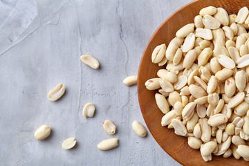 Peanuts in wooden plate isolated over white textured background, top view, close-up.