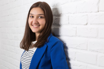 A young pretty smiling girl against a white loft-style brick wall. She looks at the viewer. Copy space.