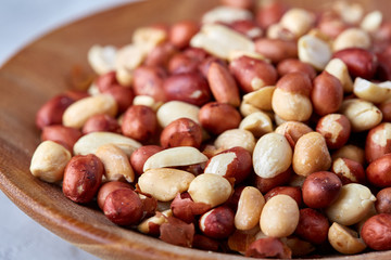 Raw mixed peanuts in wooden plate isolated over white textured background, top view, close-up.