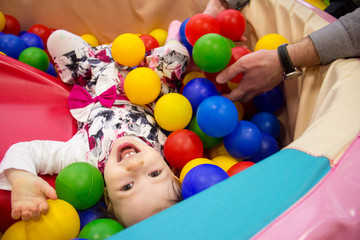 Fototapeta na wymiar Little cute smile girl plays in balls for a dry pool. Play room. Happiness. father's hand in the background