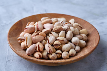 Salted pistachios on a wooden plate over white background, top view, close-up, selective focus.