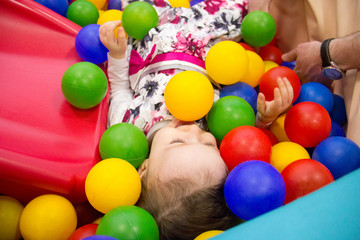 Fototapeta na wymiar Little cute smile girl plays in balls for a dry pool. Play room. Happiness. father's hand in the background